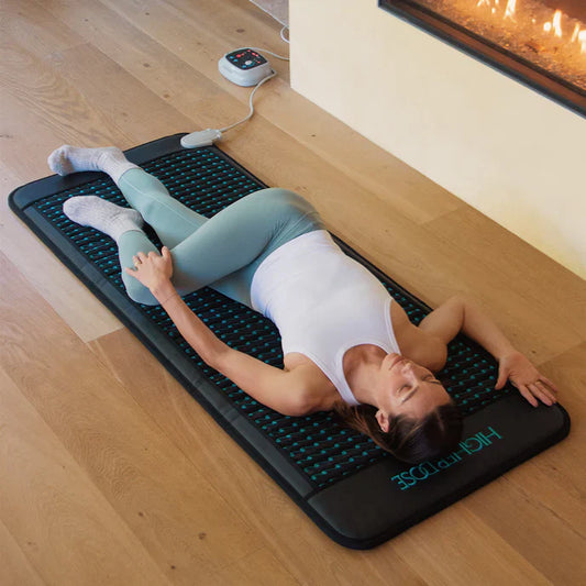 Woman relaxing on a HigherDOSE Infrared Go-Mat in a home wellness setting, part of the Guest Curated recovery ritual.