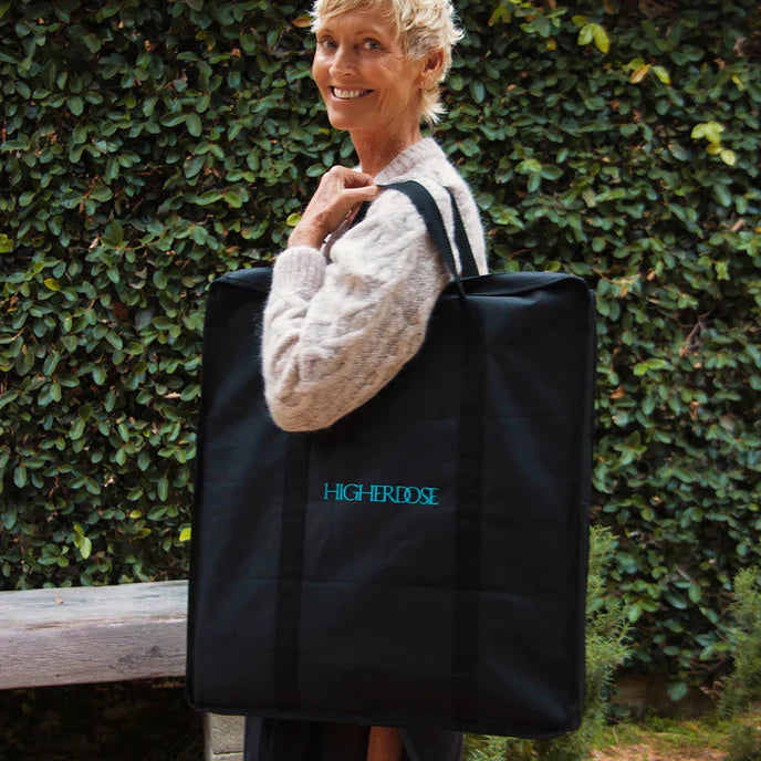 “Smiling woman carrying a large black HIGHERDOSE tote bag outdoors, luxury wellness brand accessory.